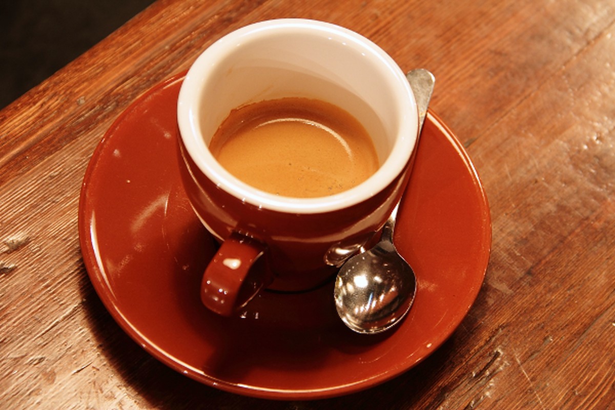 A cup of coffee on a saucer viewed from above on a warm tabletop.