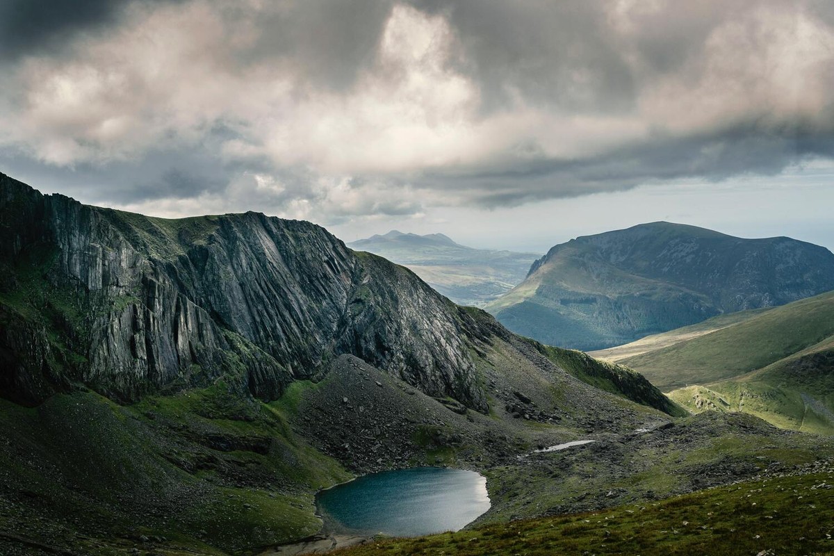 A wide mountain landscape with water, ridges, and dramatic cloud.