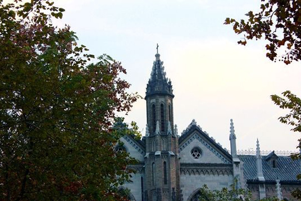 A historic building seen through leafy trees in soft daylight.